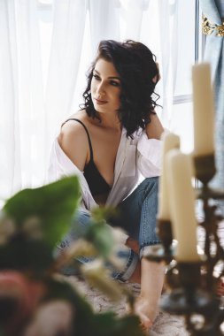 Dairelerin içinde poz veren güzel kıvırcık esmer. Mavi kot ve beyaz gömlekli genç modelin portresi. 