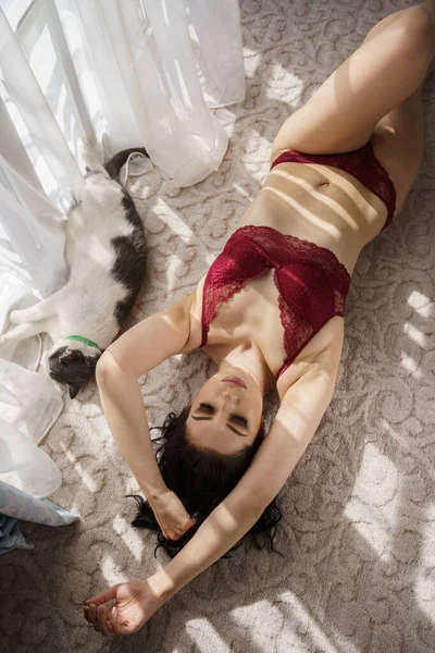 アパートのインテリアで猫と遊んで巻き毛を持つセクシーなブルネット 赤ランジェリーの若いモデルの肖像 — ストック写真