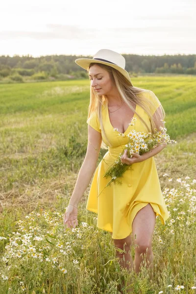 夏服の美しさブロンドの女性の屋外肖像画 昼間の花畑でポーズをとる帽子と黄色のドレスの若いモデル — ストック写真