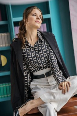 Güzel genç bir kadın kütüphanenin içinde poz veriyor. Gayri resmi giyinmiş esmer bir kadın portresi. 