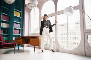 Güzel genç bir kadın kütüphanenin içinde poz veriyor. Gayri resmi giyinmiş esmer bir kadın portresi. 