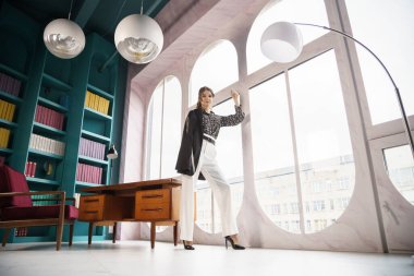 Güzel genç bir kadın kütüphanenin içinde poz veriyor. Gayri resmi giyinmiş esmer bir kadın portresi. 