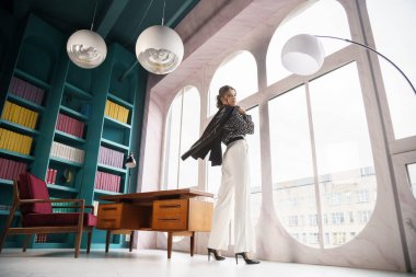 Güzel genç bir kadın kütüphanenin içinde poz veriyor. Gayri resmi giyinmiş esmer bir kadın portresi. 