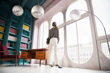 Güzel genç bir kadın kütüphanenin içinde poz veriyor. Gayri resmi giyinmiş esmer bir kadın portresi. 