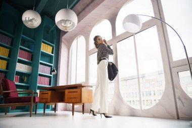 Güzel genç bir kadın kütüphanenin içinde poz veriyor. Gayri resmi giyinmiş esmer bir kadın portresi. 