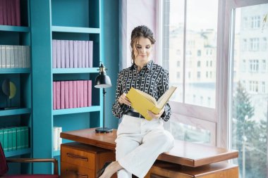 Güzel genç bir kadın kütüphanenin içinde poz veriyor. Gayri resmi giyinmiş esmer bir kadın portresi. 