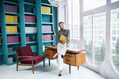 Güzel genç bir kadın kütüphanenin içinde poz veriyor. Gayri resmi giyinmiş esmer bir kadın portresi. 