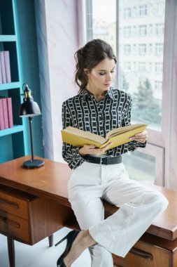 Güzel genç bir kadın kütüphanenin içinde poz veriyor. Gayri resmi giyinmiş esmer bir kadın portresi. 