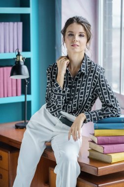 Güzel genç bir kadın kütüphanenin içinde poz veriyor. Gayri resmi giyinmiş esmer bir kadın portresi. 