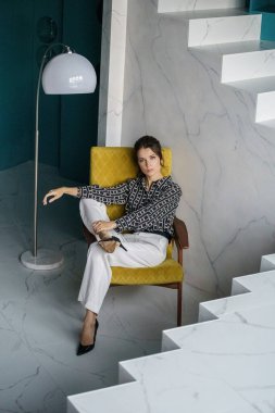 Sarı koltukta oturan güzel genç bayan. Gayri resmi giyinmiş esmer bir kadın portresi. 