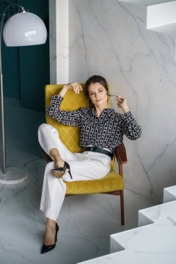 Sarı koltukta oturan güzel genç bayan. Gayri resmi giyinmiş esmer bir kadın portresi. 