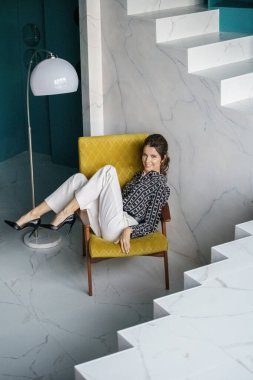 Sarı koltukta oturan güzel genç bayan. Gayri resmi giyinmiş esmer bir kadın portresi. 