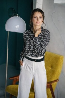 Sarı koltuğun yanında duran genç ve güzel bir kadın. Gayri resmi giyinmiş esmer bir kadın portresi. 