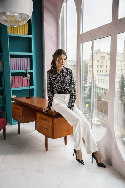 Güzel genç bir kadın kütüphanenin içinde poz veriyor. Gayri resmi giyinmiş esmer bir kadın portresi. 