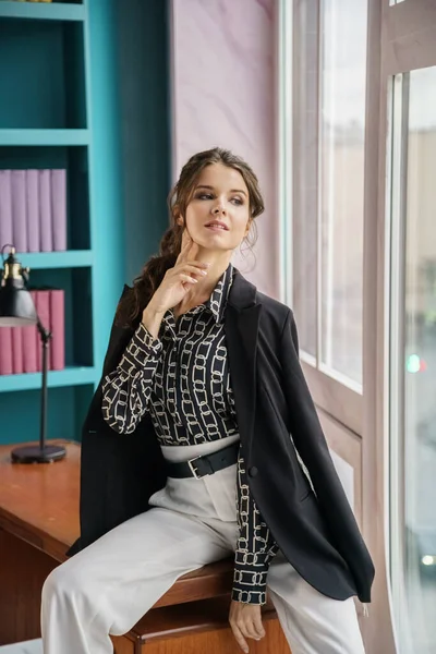 Güzel genç bir kadın kütüphanenin içinde poz veriyor. Gayri resmi giyinmiş esmer bir kadın portresi. 