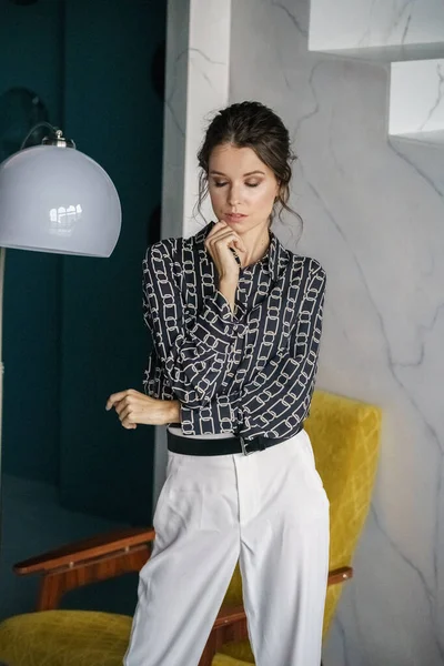 Sarı koltuğun yanında duran genç ve güzel bir kadın. Gayri resmi giyinmiş esmer bir kadın portresi. 