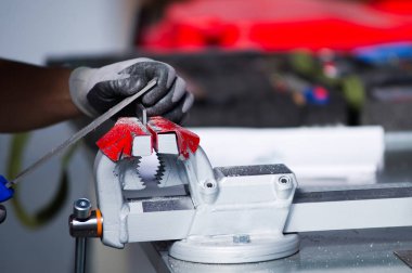 eldivenli eller bir yardımcı lıkta kenetlenmiş metal bir iş parçası üzerinde çalışır