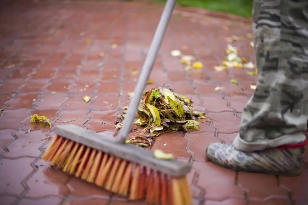 Hombre limpia con una escoba hojas de otoño de cerca — Foto de Stock