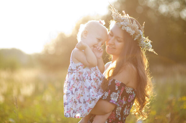 mom holds her daughter in her arms in a field at sunset