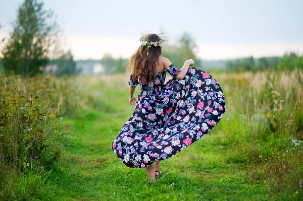 Jeune fille dans une robe de soleil colorée avec une couronne sur la tête disparaît le long d'une route — Photo