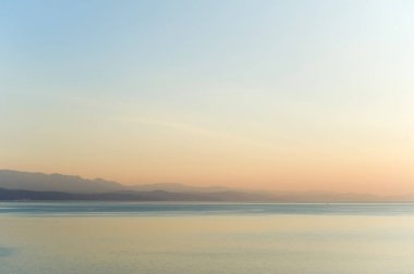 Şafakta sis, deniz ve ufuktaki dağlar.