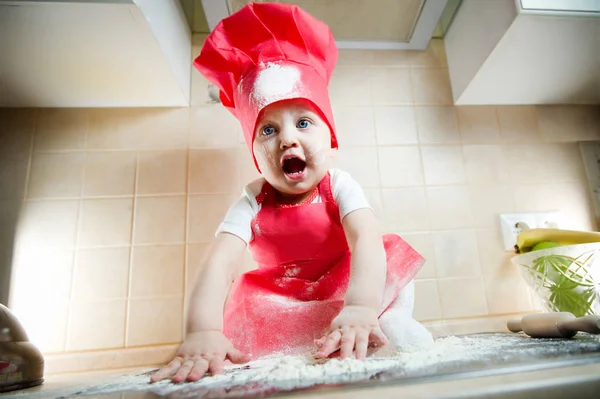 Dziewczynka w garnitur kucharz jest etnicznie krzyczeć, siedząc na piecu i grając z mąką. Mały kucharz w garniturze, dziecko — Zdjęcie stockowe