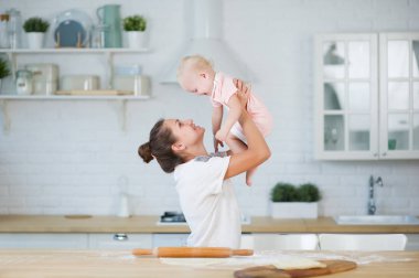 anne mutfakta küçük kızı ile oynar, uzanmış kollarında onu yukarı kaldırarak