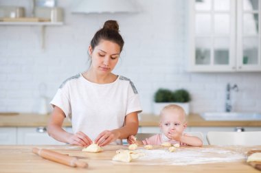 anne, bir mutfakta tezgahta duran turta heykel ve küçük bir kızı yakındaki hamur yiyor