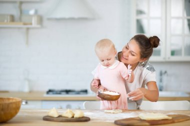 genç bir kadın arkasından küçük bir kızı kucaklar, elinde un ile ahşap bir tabak tutarak.
