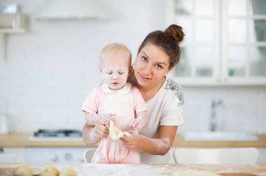 genç bir kadın elinde ahşap bir tabak tutarak, arkadan küçük bir kızı kucaklar