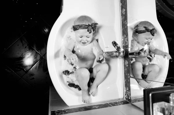 little girl splashing in a sink with milk and strawberries, squinting and smiling. Black and white shot