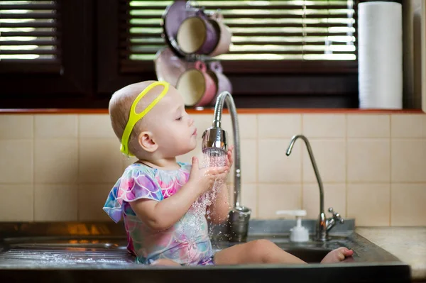 Kleines Mädchen in Badeanzug und Schwimmbrille hat Spaß in der Spüle in der Küche — Stockfoto