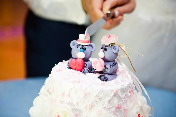 the groom and the bride carry a knife to cut the wedding cake along the line between the figures on the top