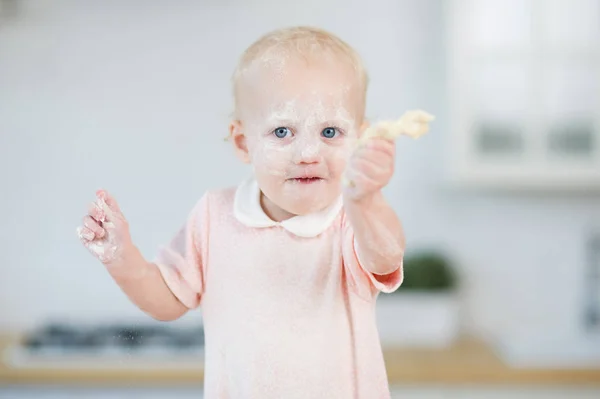 Fille aux yeux bleus avec un visage dans la farine détient un morceau de pâte — Photo