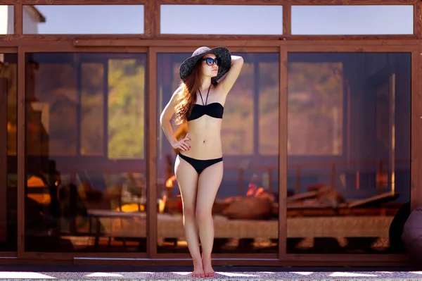 A girl in a dark hat and posing in a swimsuit near the pool — Stock Photo, Image
