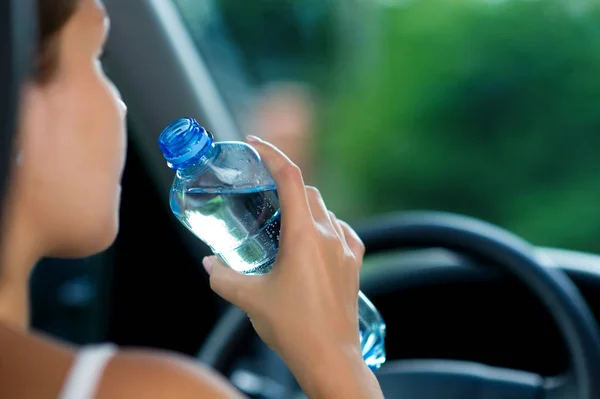 woman drives a car and is going to drink water from a bottle
