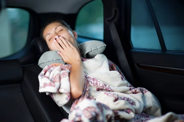 Young woman yawns, covering herself with a plaid in the back seat of a car — Stock Photo, Image
