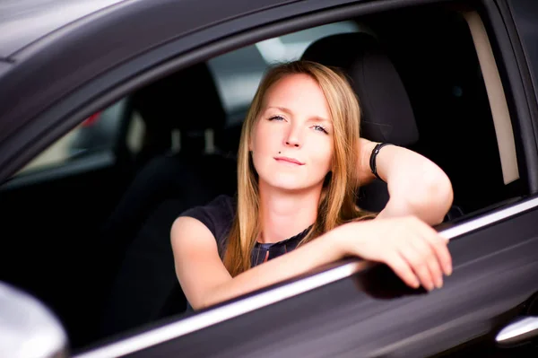 Jeune fille assise dans une voiture noire et regardant la caméra, posant — Photo