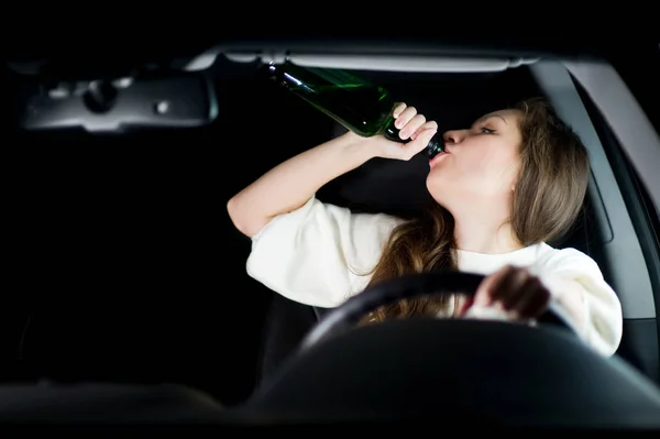 Ung kvinna dricker alkohol under körning och inte tittar på vägen — Stockfoto