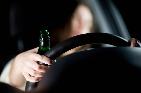 Het meisje houdt tegelijkertijd een fles alcohol en het stuur van een auto, bedreigende weggebruikers — Stockfoto