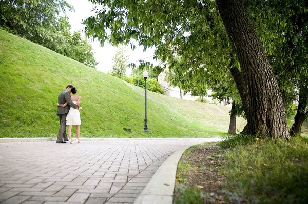Noiva e noivo estão se afastando ao longo do beco no parque, abraçando uns aos outros — Fotografia de Stock