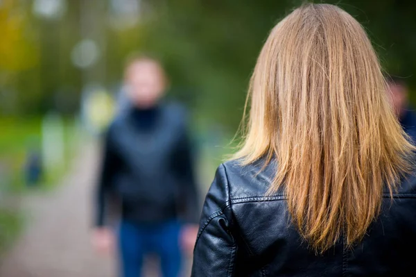 Fille dans une veste en cuir se tient avec son dos au spectateur et rencontre un homme qui est en defocus — Photo