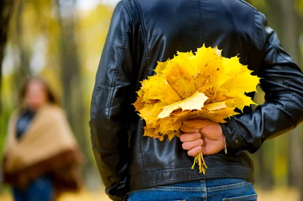 Ein Mann in Lederjacke hält einen spontanen Strauß abgefallener Blätter hinter sich. vor ihm im defokussierten Mädchen — Stockfoto