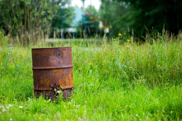 古い錆びた樽は、デフォーカスの緑の背景に対して明るい草の中に立っています — ストック写真