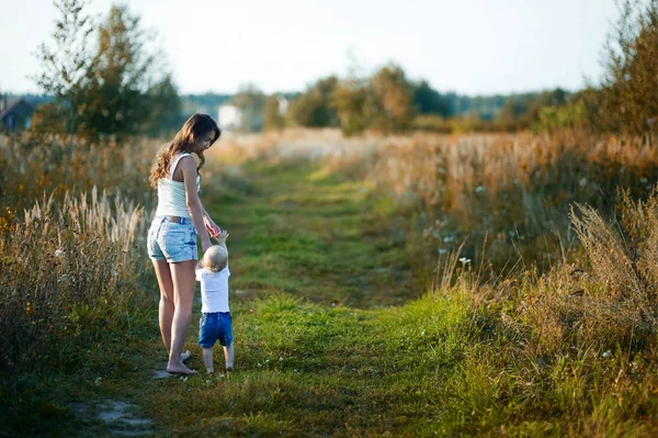 Ung mamma går med sin lilla dotter barfota på en landsväg vid solnedgången. Barnflickan går med barnet. Tonas — Stockfoto