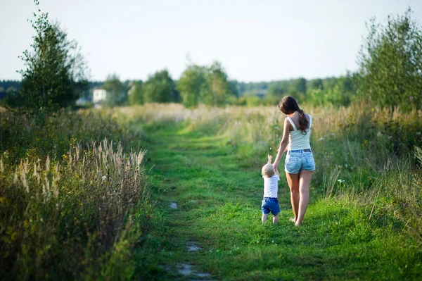 young mother walks with her little daughter barefoot on a country road at sunset, view from the back. The nanny walks with the child.