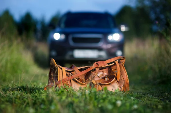Photo of an orange leather bag on a country road stretching into the distance and there is a black car in the background — Stock Photo, Image