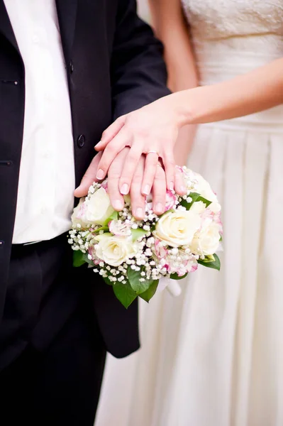 Kedua mempelai berpegangan tangan dengan cincin di atas karangan bunga — Stok Foto