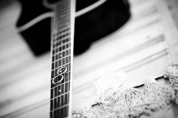 Два обручальных кольца лежат на шее акустической гитары. Черно-белый кадр — стоковое фото