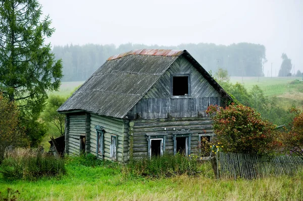 Gamla övergivna skrangliga gamla trähus utan fönster med en delvis saknas staket. Tomt täckt med gräs — Stockfoto